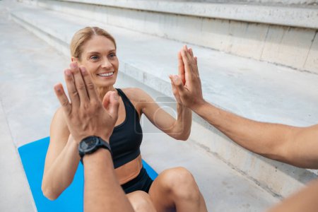 Photo for Two friends man and woman working out together and doing some crunches outdoors, touching hands. - Royalty Free Image