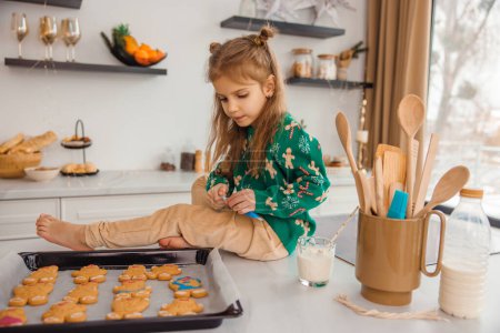 Téléchargez les photos : Cheveux longs mignon enfant assis sur la table et la préparation de biscuits au gingembre - en image libre de droit