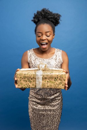 Téléchargez les photos : Joyeux jolie femme afro-américaine en robe dorée avec des cadeaux de Noël - en image libre de droit