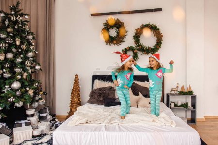 Foto de Lindos gemelos en pijama y sombreros de santa saltar en la cama - Imagen libre de derechos