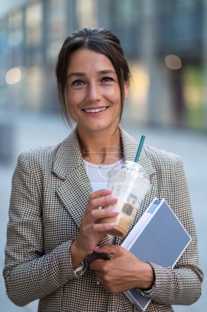 Foto de Mujer confiada sonriente que usa ropa de estilo oficial posando al aire libre bebiendo cóctel de leche y organizador de celebración. - Imagen libre de derechos