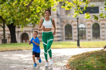 Foto de Corriendo juntos. Mujer y su hijo corriendo en el parque y mirando contentos - Imagen libre de derechos