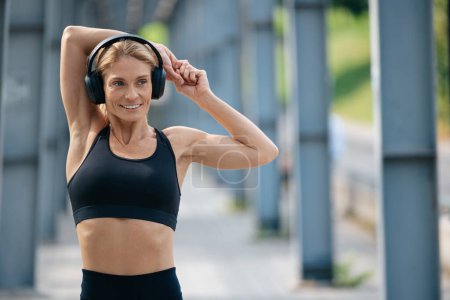 Téléchargez les photos : Femme sportive faisant des exercices de réchauffement à l'extérieur étirant les mains et écoutant de la musique. - en image libre de droit