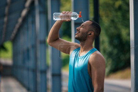 Photo for After workout. Young dark-skinned athlete pouring some refreshing water on himself after workout - Royalty Free Image