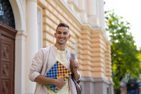 Photo for Joyful student. Smiling young man with a notebook in hands looking joyful - Royalty Free Image