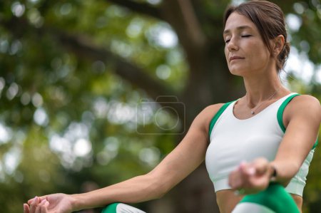 Téléchargez les photos : Méditation. Femme en tenue de sport verte assise dans une pose de lotus et méditant - en image libre de droit