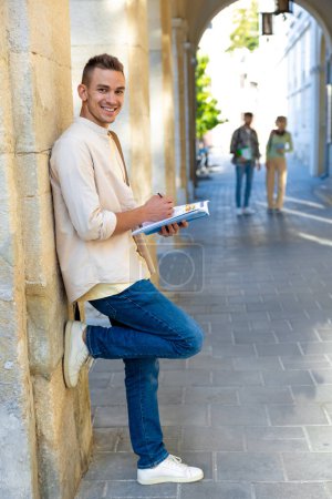 Photo for Student. Handsome young man standing near the wall with a textbook in hands - Royalty Free Image