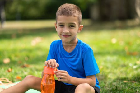 Photo for Water balance. Cute boy in blue tshirt with orange bottle in hands - Royalty Free Image