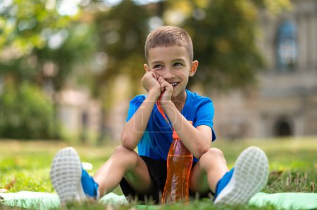 Photo for Summer day. Boy in blue tshirt sitting on the grass and looking aside - Royalty Free Image