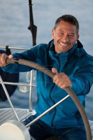 Photo for On the yacht. Good-looking mature man sailing a yacht and looking confident - Royalty Free Image