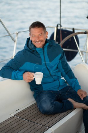 Foto de Un hombre en un yate. Hombre de chaqueta azul en el yate tomando café y mirando satisfecho - Imagen libre de derechos