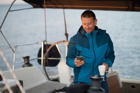 Photo for Man on a yacht. Man in blue jacket on the yacht having coffee and looking contented - Royalty Free Image