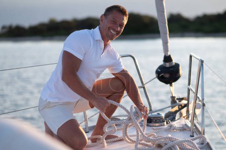 Téléchargez les photos : Avant de naviguer. Homme souriant sur un yacht fixant la corde - en image libre de droit