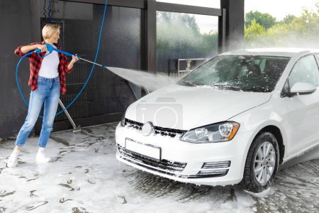 Téléchargez les photos : Femme en chemise rouge nettoyant la voiture avec un tuyau - en image libre de droit