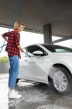 Photo for Car wash. Woman with a hose in hands washing the car - Royalty Free Image