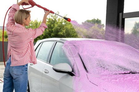 Téléchargez les photos : Nettoyage de la voiture. Femme blonde laver la voiture avec une mousse colorée - en image libre de droit
