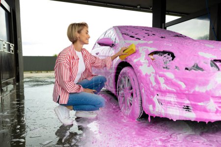 Photo for Cleaning the car. Blonde woman washing the car with a colorful foam - Royalty Free Image