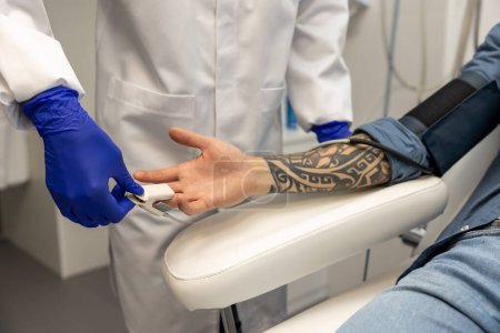 Foto de Enfermera midiendo presión y nivel de oxígeno en dedo masculino en clínica. - Imagen libre de derechos
