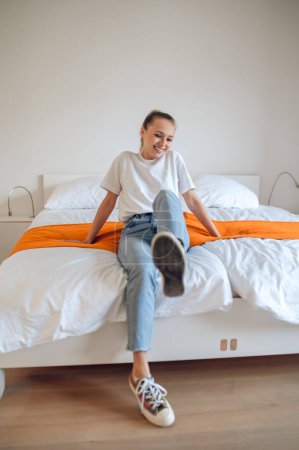 Foto de Me siento bien. Chica joven en jeans y camiseta blanca divirtiéndose en el dormitorio - Imagen libre de derechos