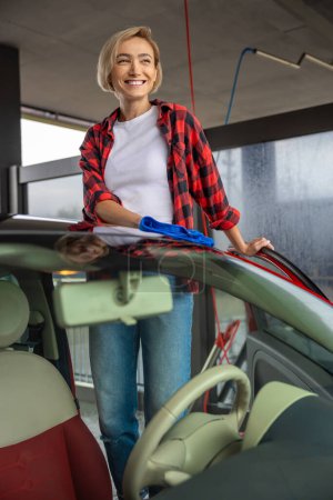 Téléchargez les photos : Service de voiture. Jeune femme souriante nettoyer la voiture et se sentir bien - en image libre de droit