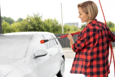 Foto de Mujer en camisa roja limpiando el coche en el lavado de coches - Imagen libre de derechos