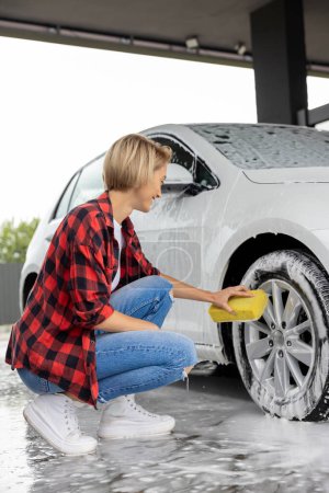 Photo for Washing a car. Blonde woman in checkered shirt washing a white car - Royalty Free Image