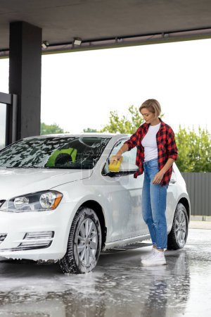 Photo for Car washing. Blonde young woman washing car windscreen and looking involved - Royalty Free Image