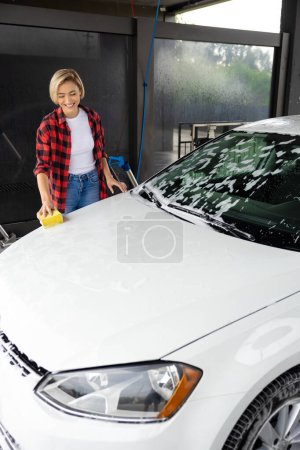 Téléchargez les photos : Lavage de voiture. Travailleur lavage de voiture nettoyage de la voiture blanche - en image libre de droit