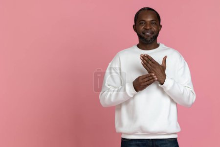 Téléchargez les photos : Sourd muet noir homme portant sweat-shirt blanc gestuelle langue des signes isolé sur fond rose. - en image libre de droit