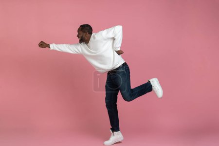 Téléchargez les photos : Homme noir excité portant un sweat blanc volant comme un super-héros isolé sur fond rose. - en image libre de droit