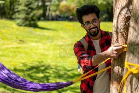 Photo for Man in checkered shirt tying ropes to the tree and adjusting hammock - Royalty Free Image