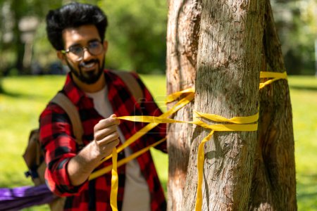 Téléchargez les photos : Homme en chemise à carreaux attachant des cordes à l'arbre et ajustant l'hamac - en image libre de droit
