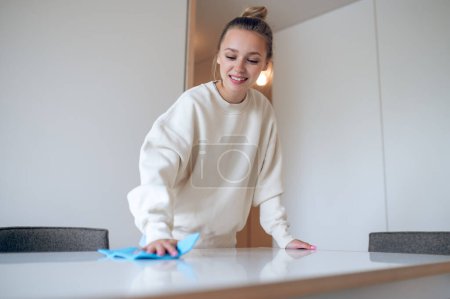 Téléchargez les photos : Jeune femme au foyer en sweat-shirt blanc nettoyant sa maison et essuyant la poussière. - en image libre de droit