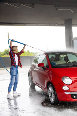 Foto de Limpieza de autos. Mujer joven con camisa a cuadros lavando un coche - Imagen libre de derechos