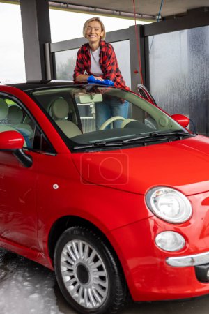 Téléchargez les photos : Nettoyage de voiture. Femme en chemise à carreaux rouges essuyant la voiture avec une serviette - en image libre de droit