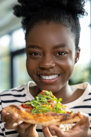 Photo for Pretty young dark-skinned woman eating pizza and feeling good - Royalty Free Image