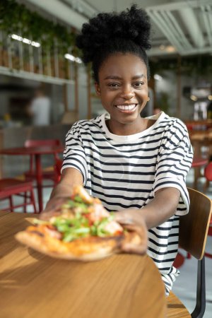 Foto de Mujer de piel oscura bastante joven comiendo pizza y sintiéndose bien - Imagen libre de derechos