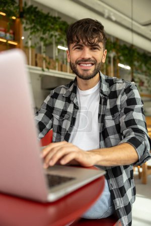 Foto de Joven hombre sonriente trabajando en el ordenador portátil en un café - Imagen libre de derechos