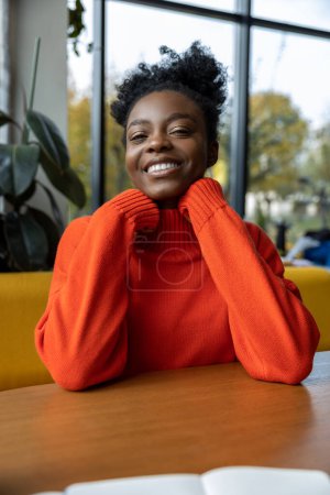 Foto de Mujer joven positiva de piel oscura en suéter de cuello redondo naranja - Imagen libre de derechos