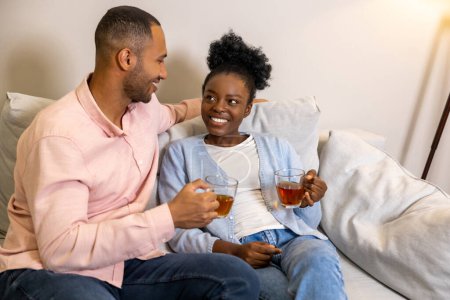Photo for Delighted man and woman enjoying hot tea and pleasant conversation while sitting together on couch - Royalty Free Image