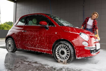 Téléchargez les photos : Lavage de voiture. Blonde jeune femme laver une voiture et se sentir positive - en image libre de droit