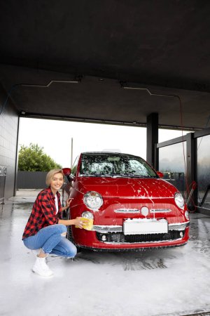 Photo for Car wash. Blonde young woman washing a car and feeling positive - Royalty Free Image