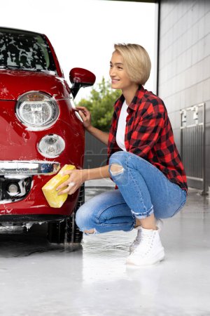 Téléchargez les photos : Lavage de voiture. Blonde jeune femme laver une voiture et se sentir positive - en image libre de droit