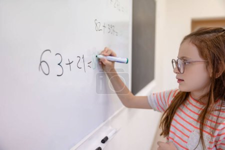Photo for Little schoolgirl counting math equation on whiteboard in school. - Royalty Free Image