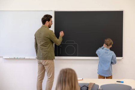 Foto de Pequeño alumno de pie en el aula mientras aprende la lección de matemáticas con su profesor. - Imagen libre de derechos