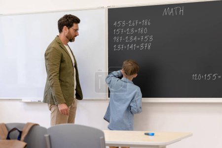 Téléchargez les photos : Enseignant masculin travaillant avec un élève lors d'une leçon de résolution de tâches mathématiques en classe à l'école. - en image libre de droit