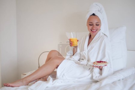 Photo for Breakfast. Cute young woman in bath robe having breakfast and feeling enjoyed - Royalty Free Image