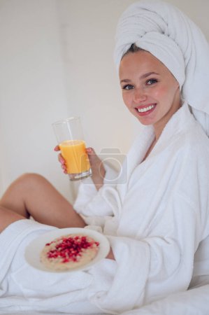 Téléchargez les photos : Petit déjeuner. Jeune femme mignonne en peignoir de bain prendre le petit déjeuner et se sentir apprécié - en image libre de droit