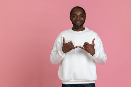 Foto de Hombre negro con sudadera blanca usando lenguaje de señas aislado sobre fondo rosa. - Imagen libre de derechos