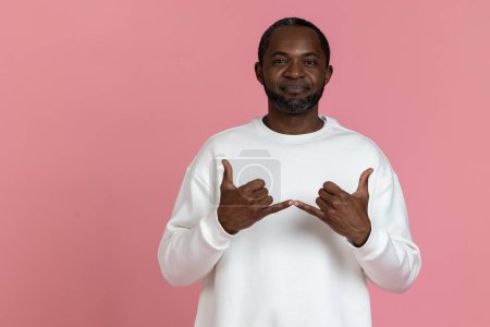 Téléchargez les photos : Homme noir portant un sweat blanc utilisant le langage des signes isolé sur fond rose. - en image libre de droit